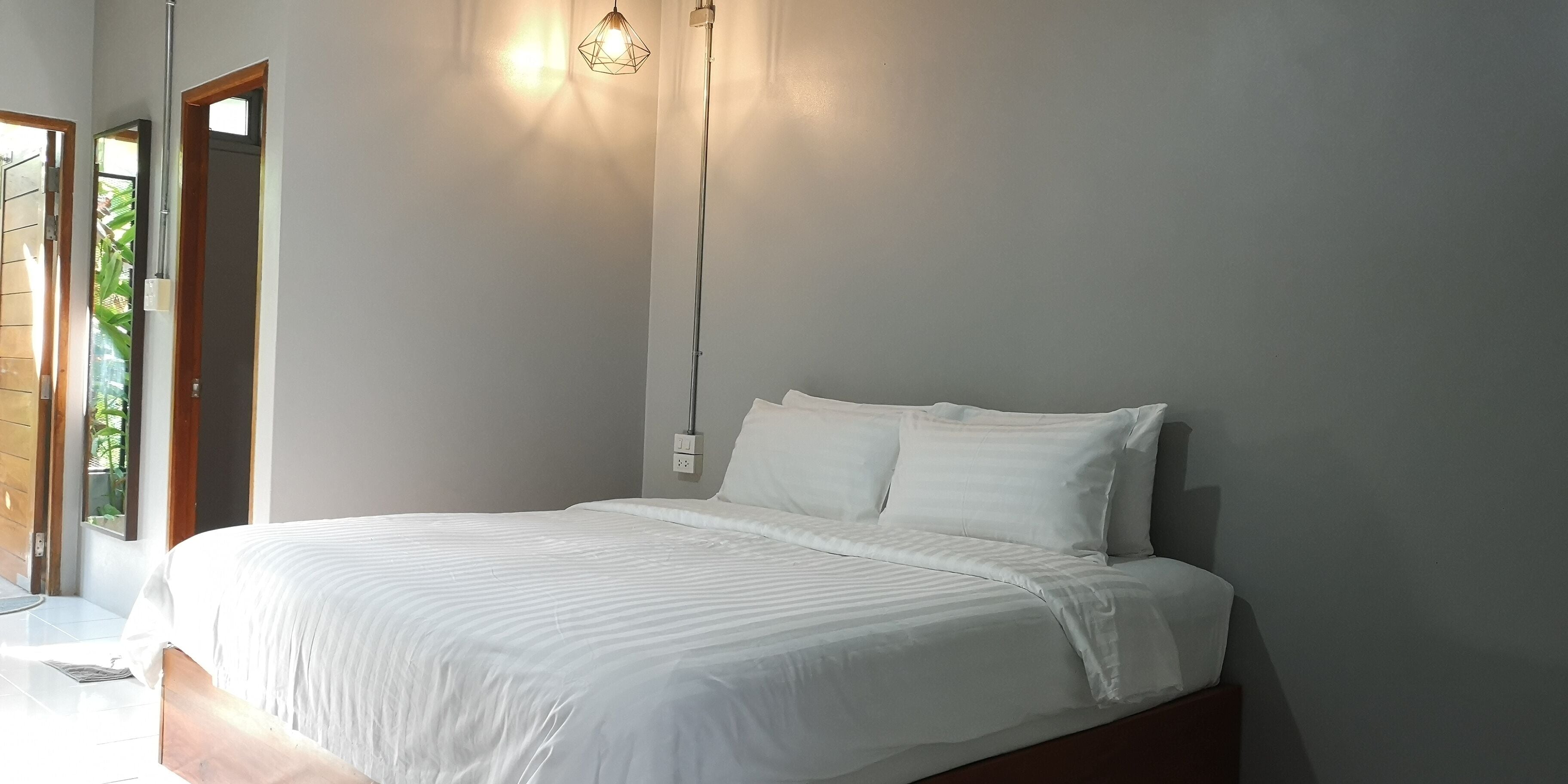 A bedroom with a bed, a nightstand, a wall-mounted lamp, and a door leading to a balcony.
