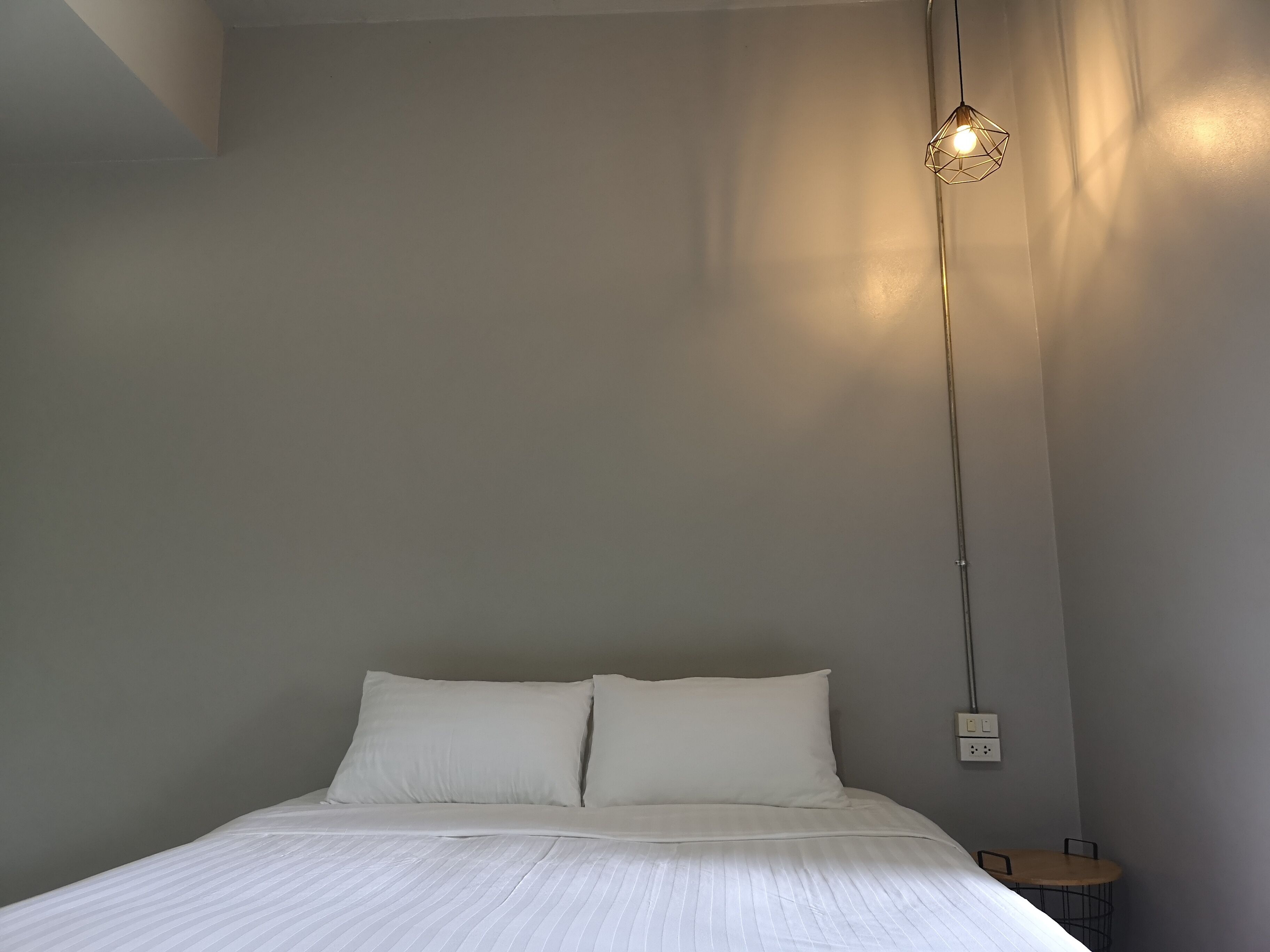 Une chambre à coucher avec un lit, deux oreillers, un luminaire suspendu et une petite table avec une chaise.