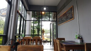 L’intérieur d’un restaurant, avec de grandes fenêtres, des tables en bois et un menu écrit à la craie sur un tableau noir.