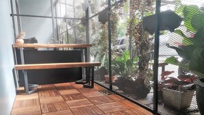 Un banc en bois et une plante en pot se trouvent dans une pièce dont le mur est fait d’un treillis et le sol, de planches de bois.