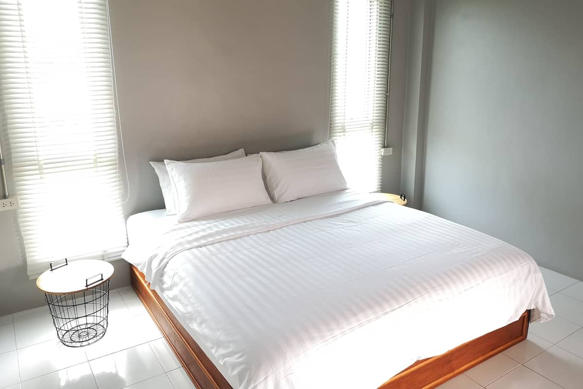 Una cama bien hecha con ropa blanca en una habitación con paredes grises claros y suelo de baldosas blancas.