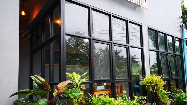 Un bâtiment doté de grandes fenêtres et d’une rangée de plantes en pot devant l’entrée.