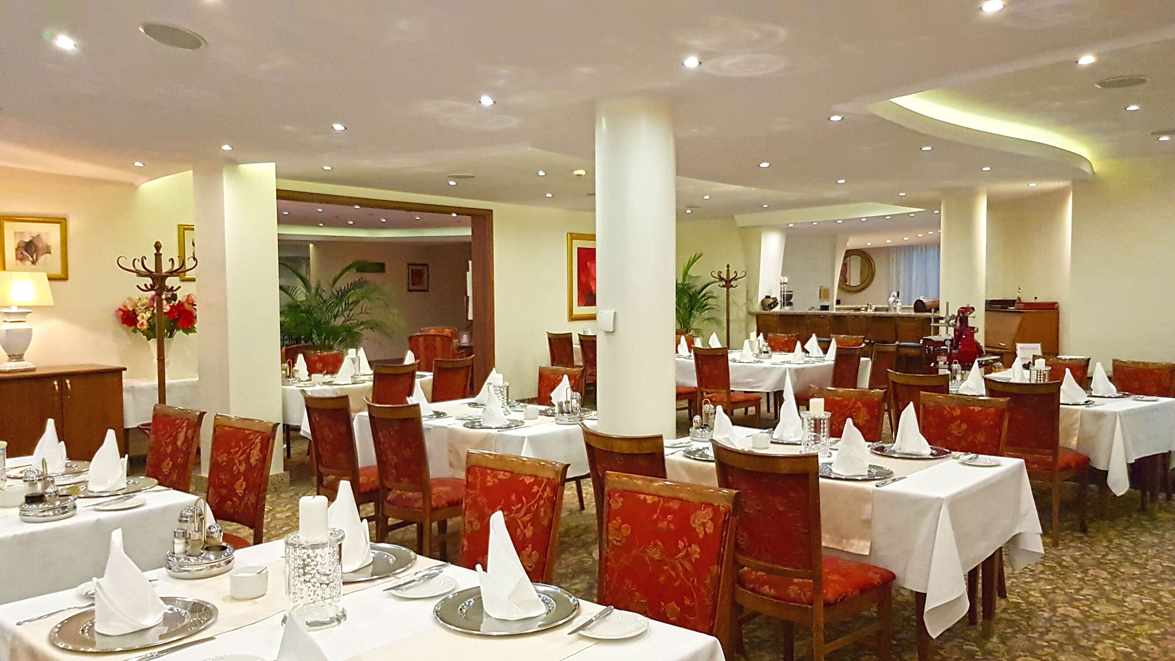 Un restaurante con varias mesas dispuestas para comer, con manteles blancos y sillas tapizadas en rojo.