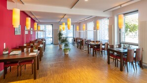 A modern dining area with wooden tables and chairs, large windows, and pendant lighting. - Hotel NeuHaus (Dortmund)