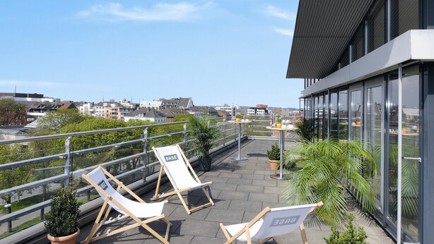 A rooftop terrace with lounge chairs, potted plants, and a view of the cityscape. - Hotel NeuHaus (Dortmund)