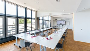 A modern conference room with large windows, white tables, and grey chairs. - Hotel NeuHaus (Dortmund)