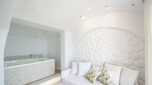 A modern bathroom with a freestanding bathtub, a white sofa with cushions, and a textured wall. - Cyano Suites (Naxos)