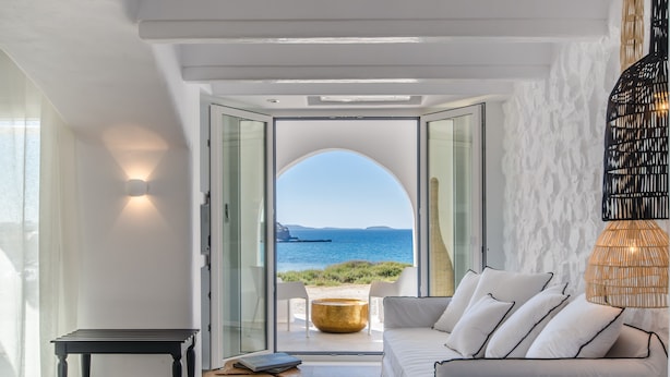 A modern interior with a sofa, a table, and a view of the sea through an arched doorway. - Cyano Suites (Naxos)