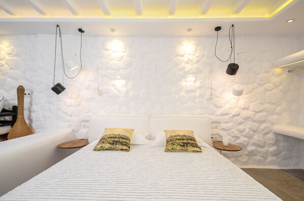 A modern bedroom with a white textured wall, a bed with patterned pillows, and a bedside table with a vase.
