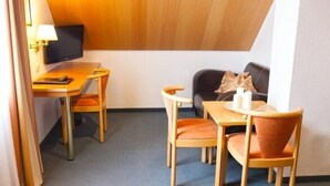 A compact room with a desk, two chairs, a sofa, and a television. - Hotel Am Ostpark (Munich)
