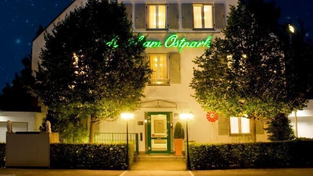 A two-story building with a green neon sign reading "Am Osterreich" and three stars above the entrance. - Hotel Am Ostpark (Munich)