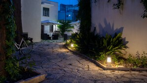 A stone-paved courtyard with a bicycle, outdoor seating, and ambient lighting. - Villa Domus Salento Suites & Rooms (Lecce)