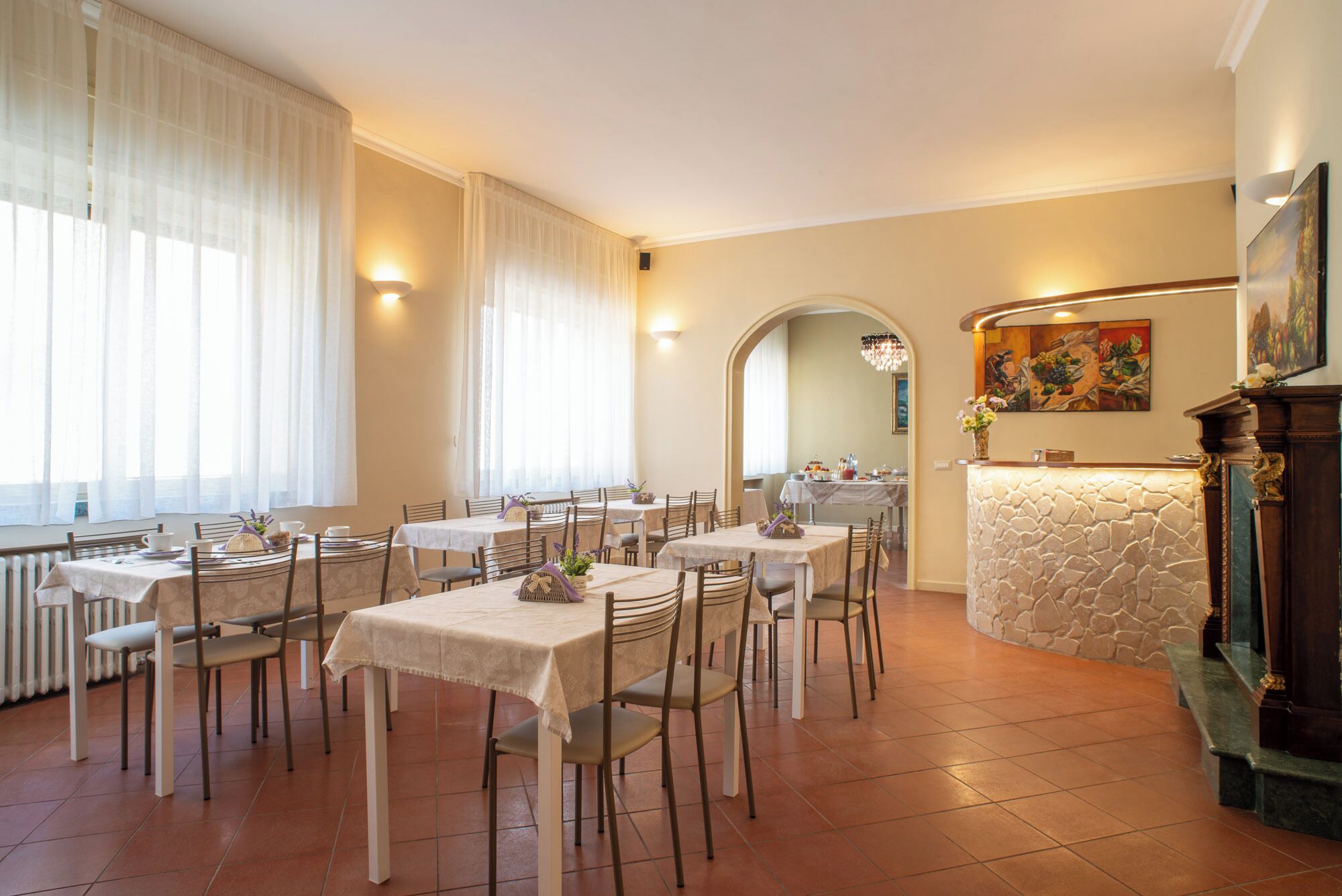Un restaurant avec plusieurs tables et chaises, un comptoir d’accueil en pierre et un tableau accroché au mur.