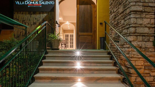 A staircase leading to a building entrance with a stone wall on the right and a green railing on the left. - Villa Domus Salento Suites & Rooms (Lecce)