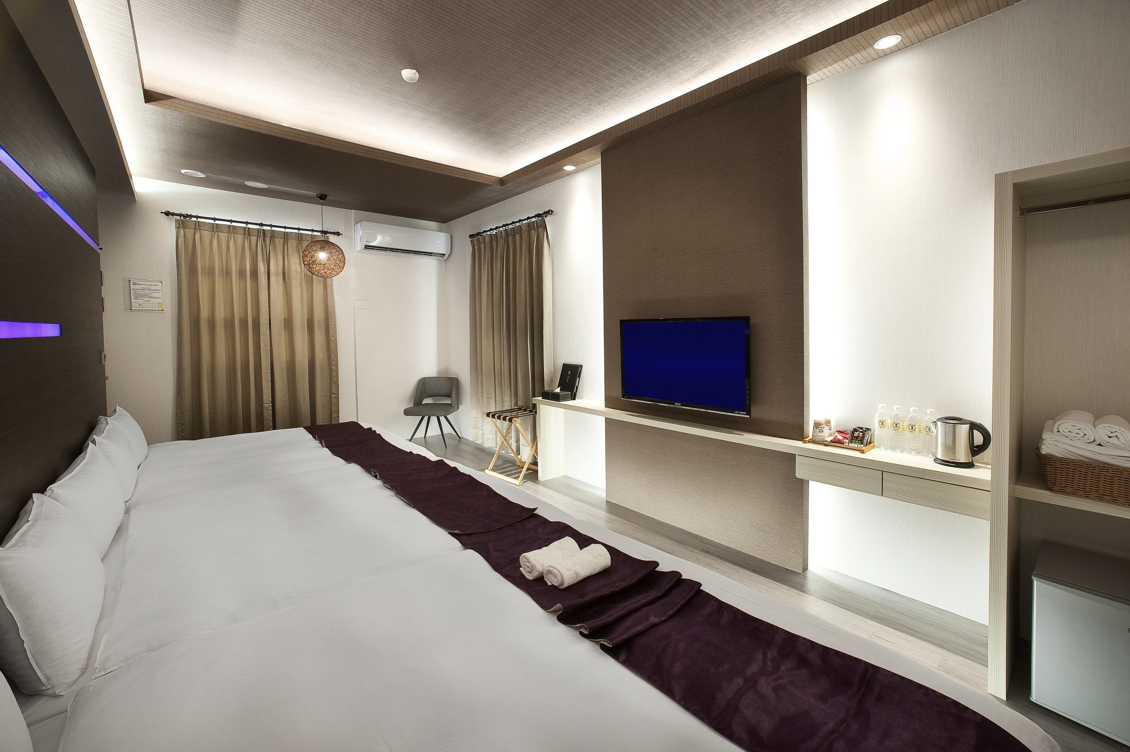 Una habitación de hotel moderna con una cama grande, televisión, escritorio y minibar.