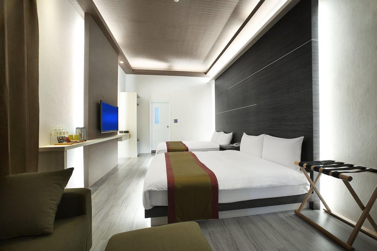 A modern hotel room with a large bed, a TV, a desk, and a seating area.