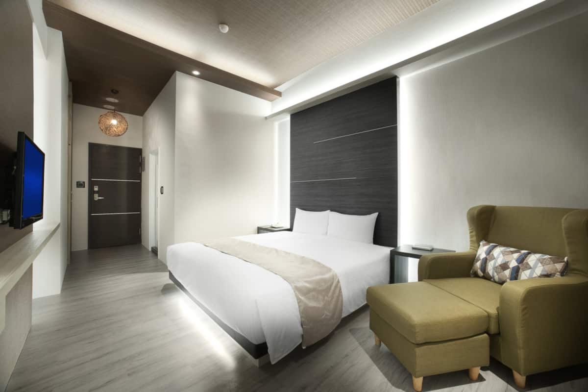 A modern hotel room with a large bed, a sofa, a television, and a dark accent wall.
