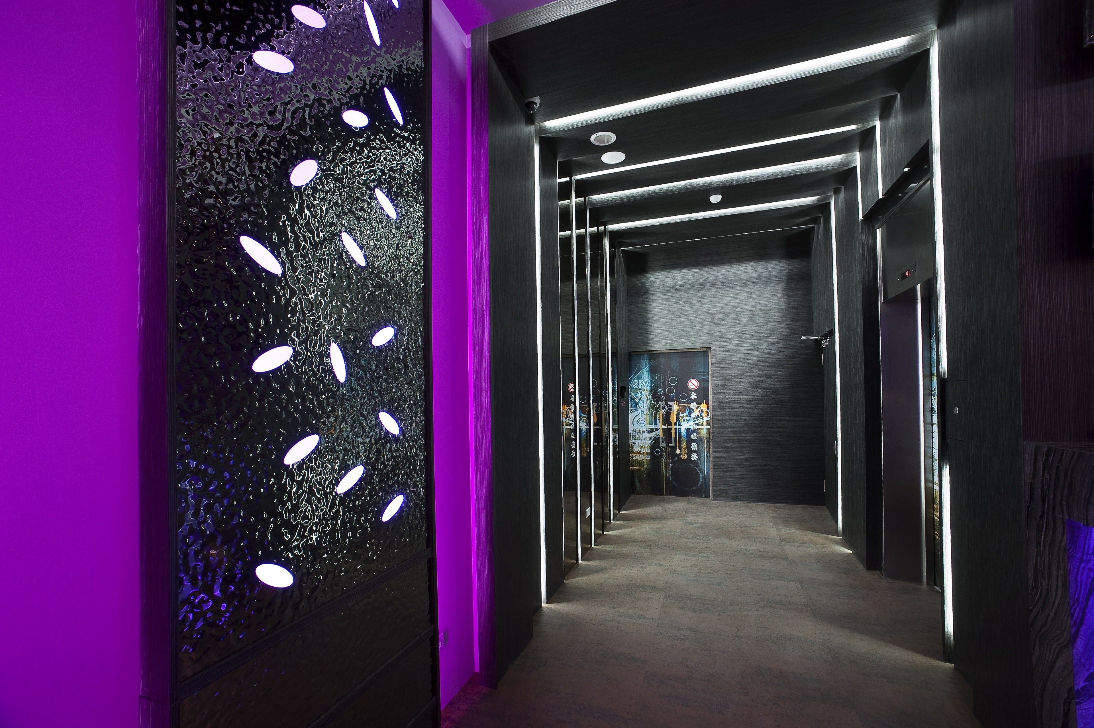 A modern hallway with a reflective wall and a purple-lit door.