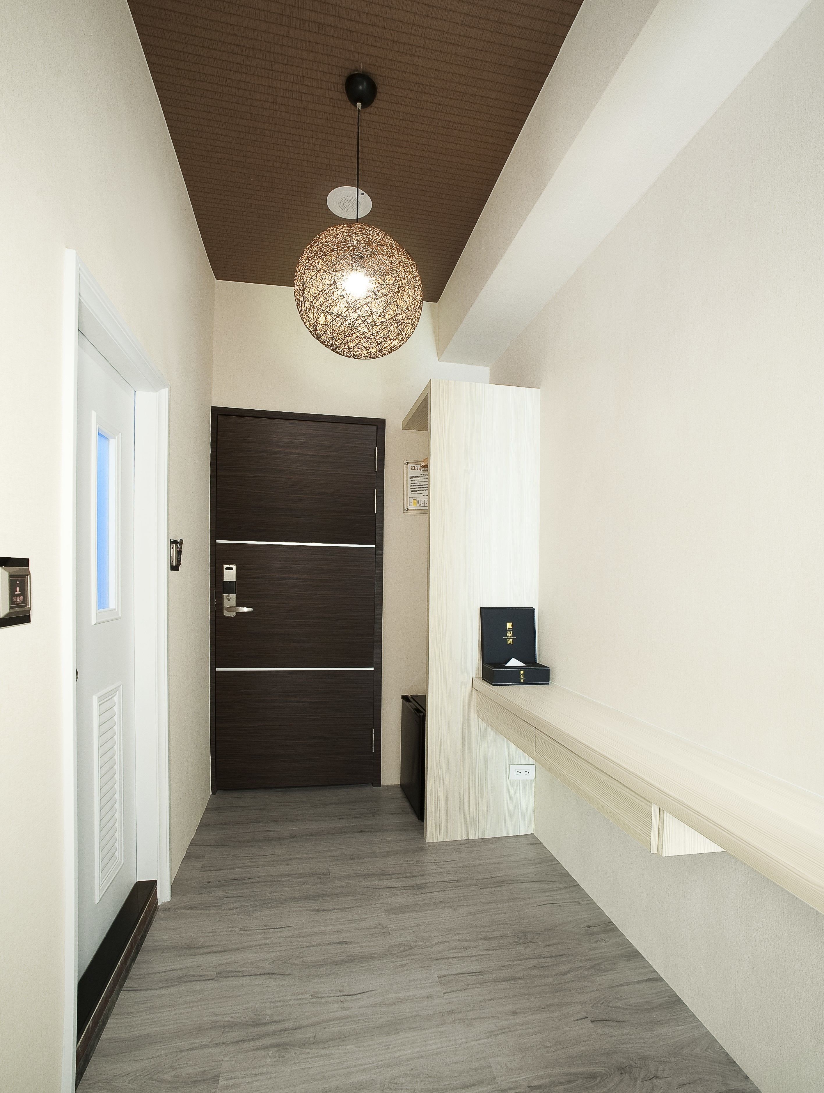 A hallway with a dark wooden door, a white wall with a bulletin board, and a hanging light fixture.