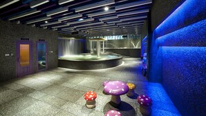 Un espacio interior moderno con una fuente de agua, una zona de estar circular y taburetes con forma de hongo de colores.