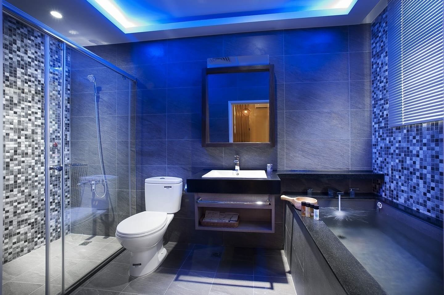 A modern bathroom with a glass-enclosed shower, a white toilet, a sink with a mirror above, and a tiled wall with a blue hue.