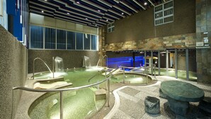 Un área de spa con varios jacuzzis, paredes de piedra y un diseño de techo moderno.