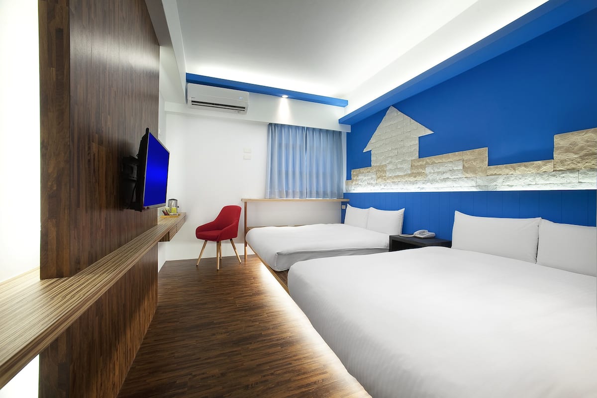 A hotel room with two beds, a wooden reception desk, a red chair, and a blue accent wall.