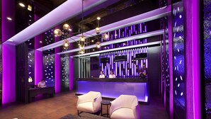 Un vestíbulo moderno con una mesa de recepción, dos sillones blancos y una zona de bar con tiras de luz verticales.