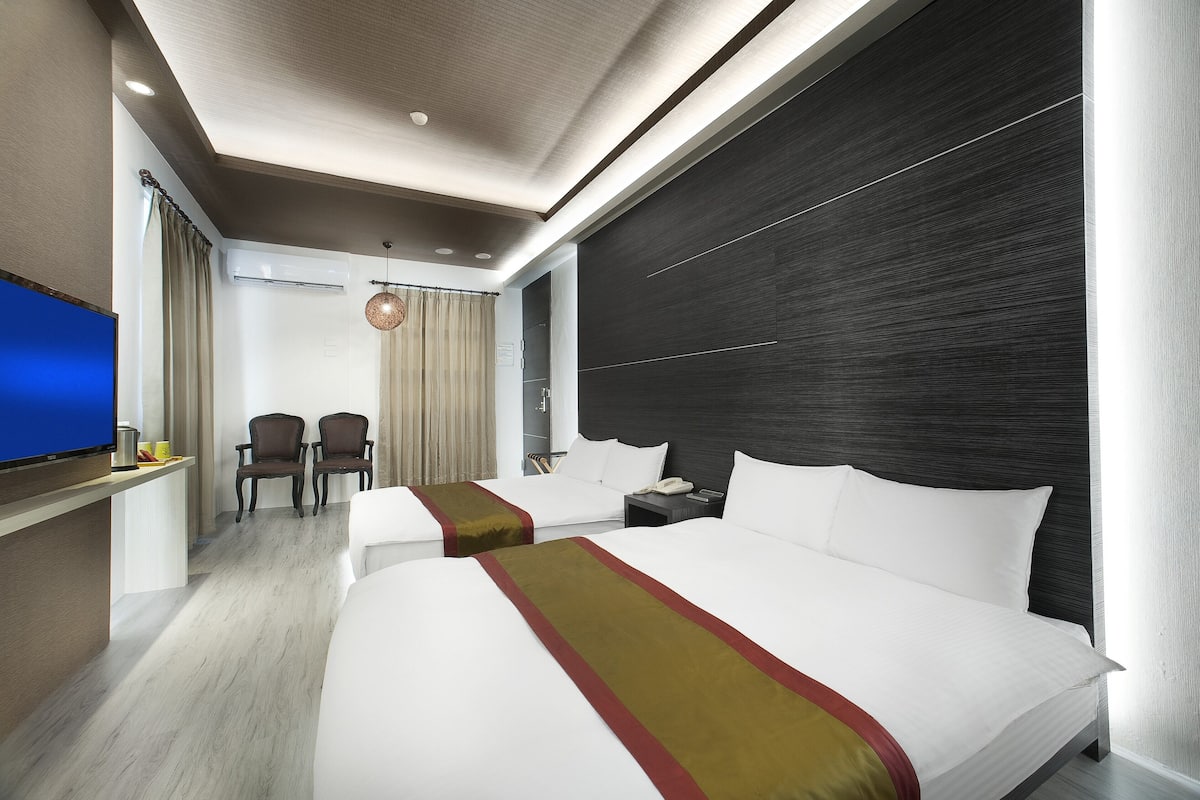 A modern hotel room with two beds, a flat-screen TV, a desk with a chair, and a minibar.