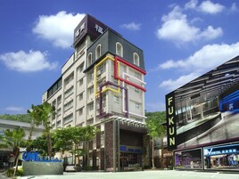 Un hotel de varios pisos con un letrero llamativo que dice 'FUKUN HOTEL' y un letrero que indica un establecimiento cercano llamado 'ONE'.