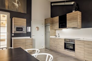 Una cocina moderna con electrodomésticos integrados, un comedor con mesa y sillas, y un amplio ventanal que proporciona luz natural.