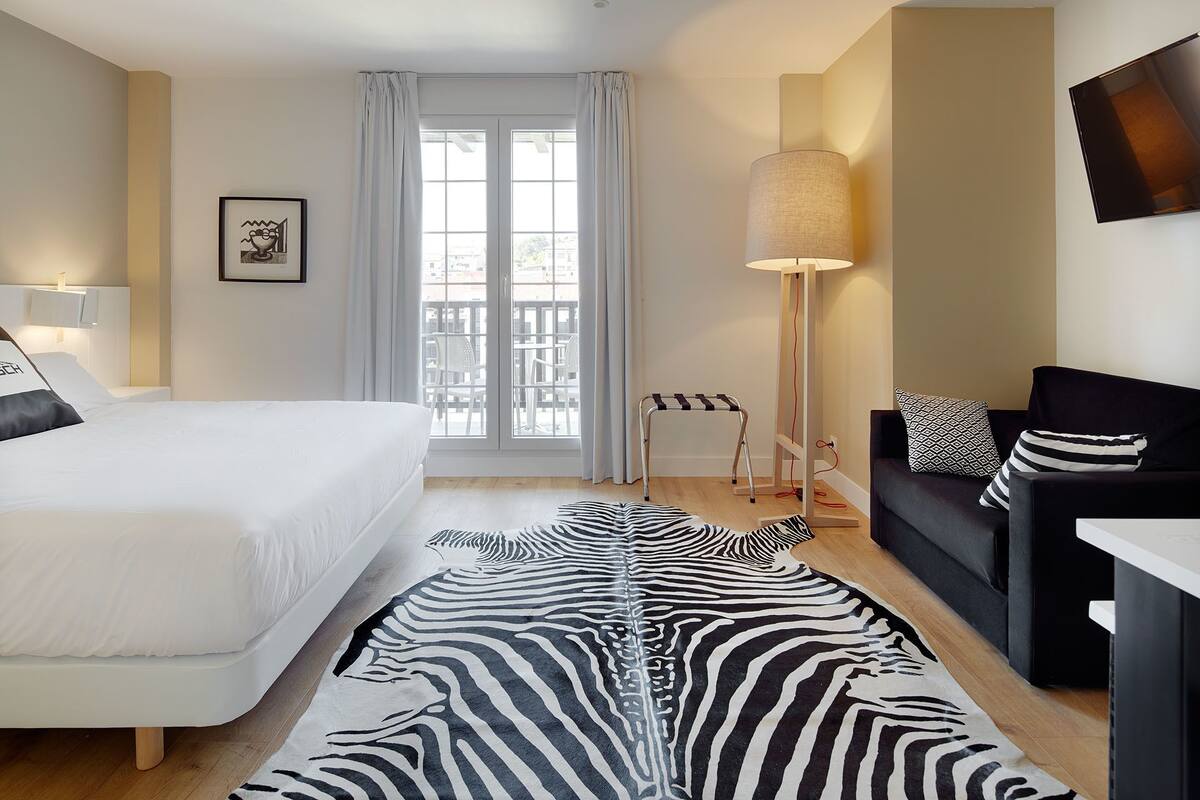 Une chambre d’hôtel avec un lit, un canapé, une lampe sur pied et un tapis à motifs zébrés.