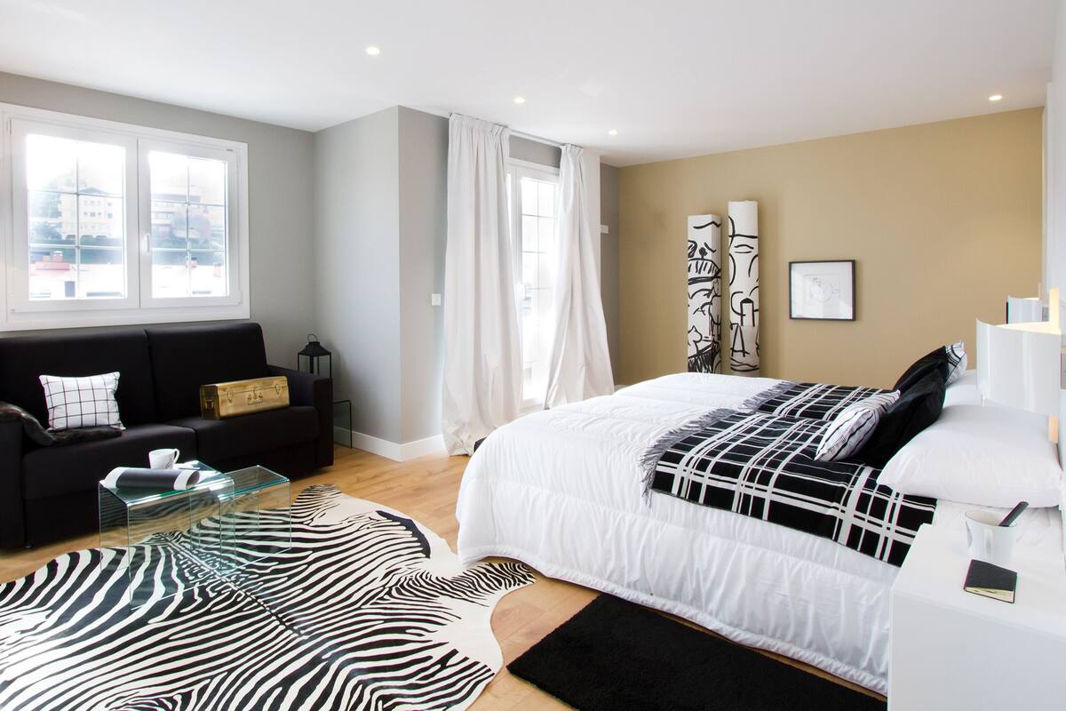 Une chambre moderne avec un lit, un canapé, une table basse en verre et un tapis à motifs zébrés.