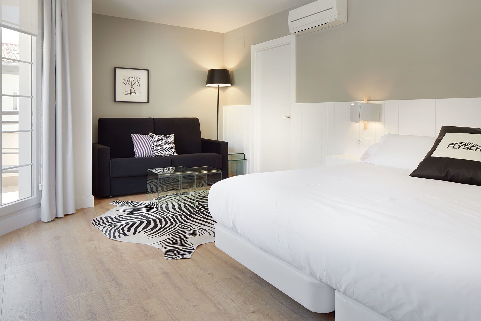 A modern hotel room with a large bed, a sofa, a glass coffee table, and a zebra print rug.