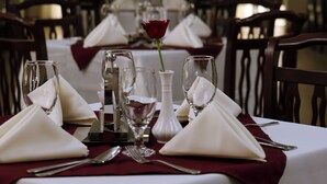 A long dining table set with white tablecloths, red napkins, and a single red rose centerpiece. - Haile Hotel Shashemene (Shashamane)