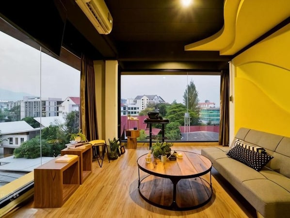 Un salon moderne avec une table basse ronde, un canapé et une vue sur le paysage urbain grâce à de grandes fenêtres.