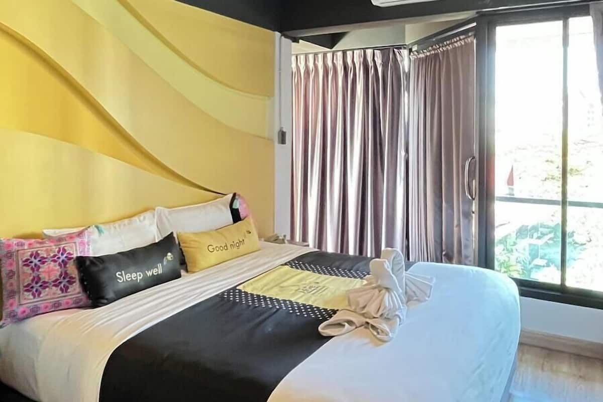 Habitación de hotel con cama, almohadas, toalla y vistas a través de una ventana con cortinas.