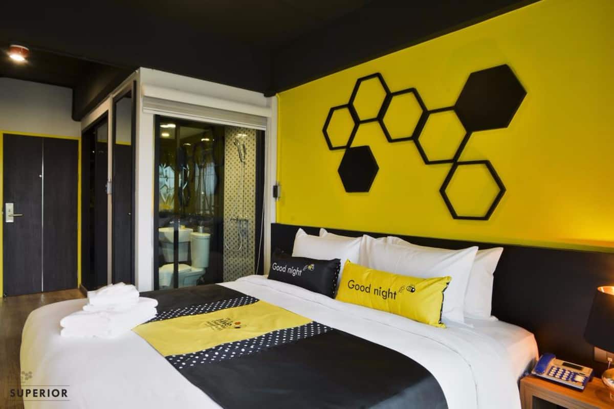 Una habitación de hotel moderna con una cama, un diseño de pared amarillo y negro, y un ventanal que da a un balcón.