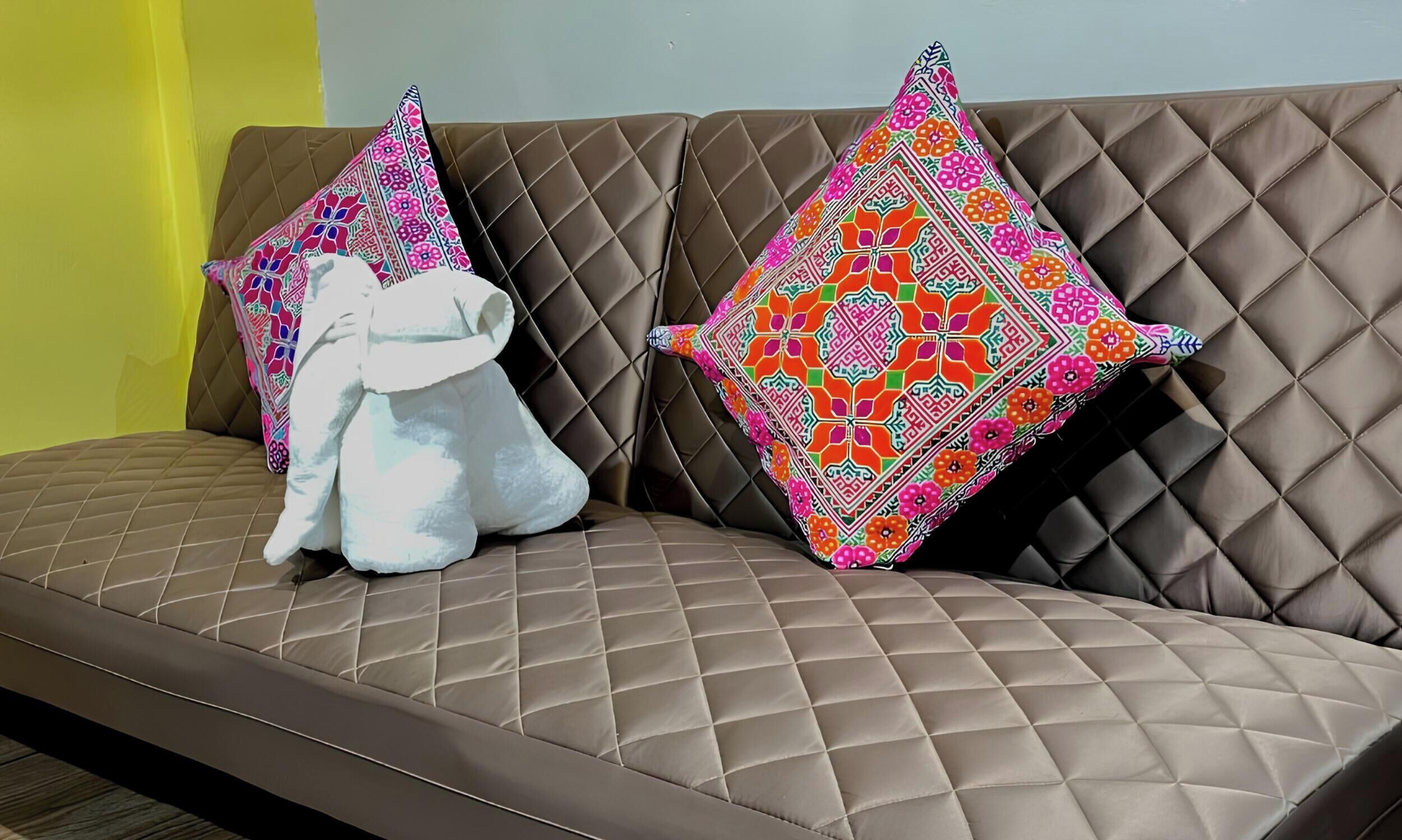 Ein braunes, gepolstertes Sofa mit zwei Zierkissen, eines mit Blumenmuster und das andere mit geometrischem Design.