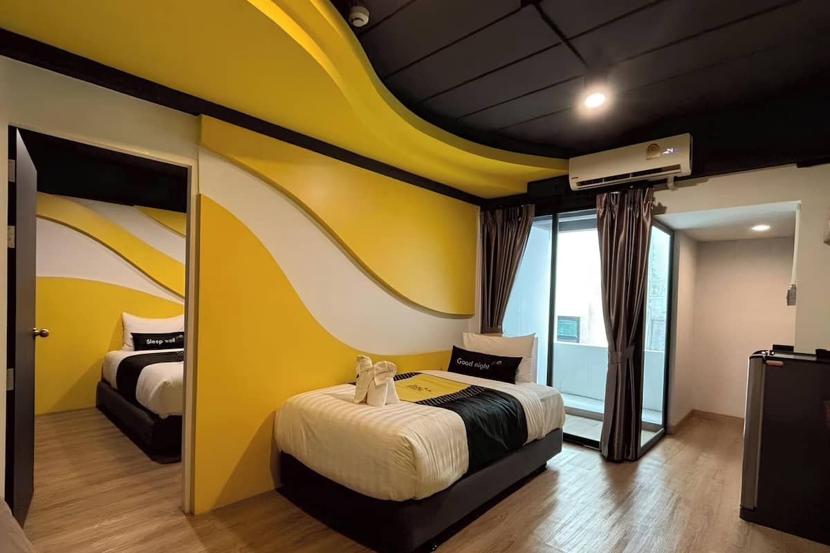 Habitación de hotel moderna con una pared curva de color amarillo, una cama grande con cabecera blanco y negro, una zona de estar separada y un amplio ventanal con cortinas.