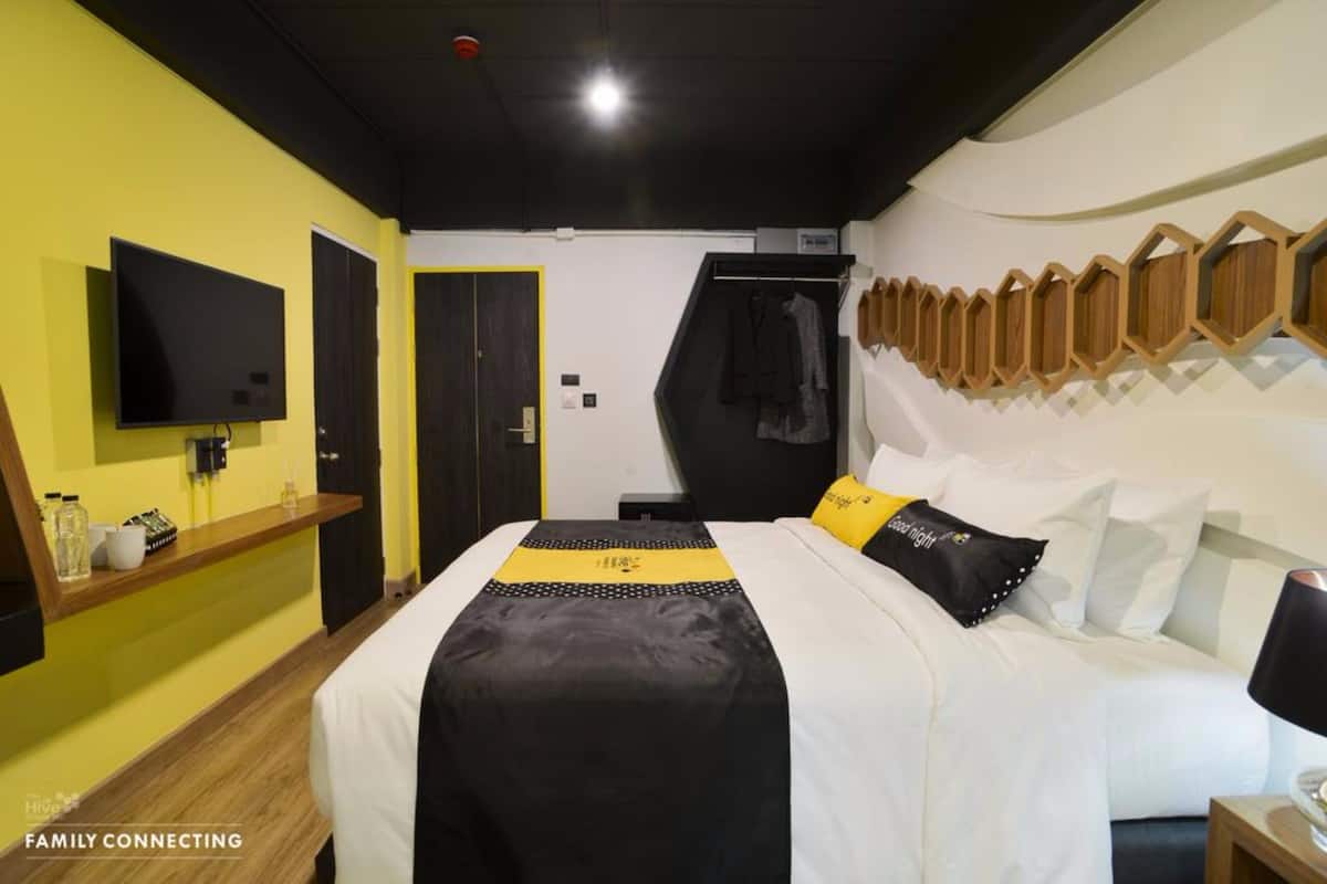 Habitación de hotel con cama, televisor, estante con artículos de aseo y perchero en la pared.
