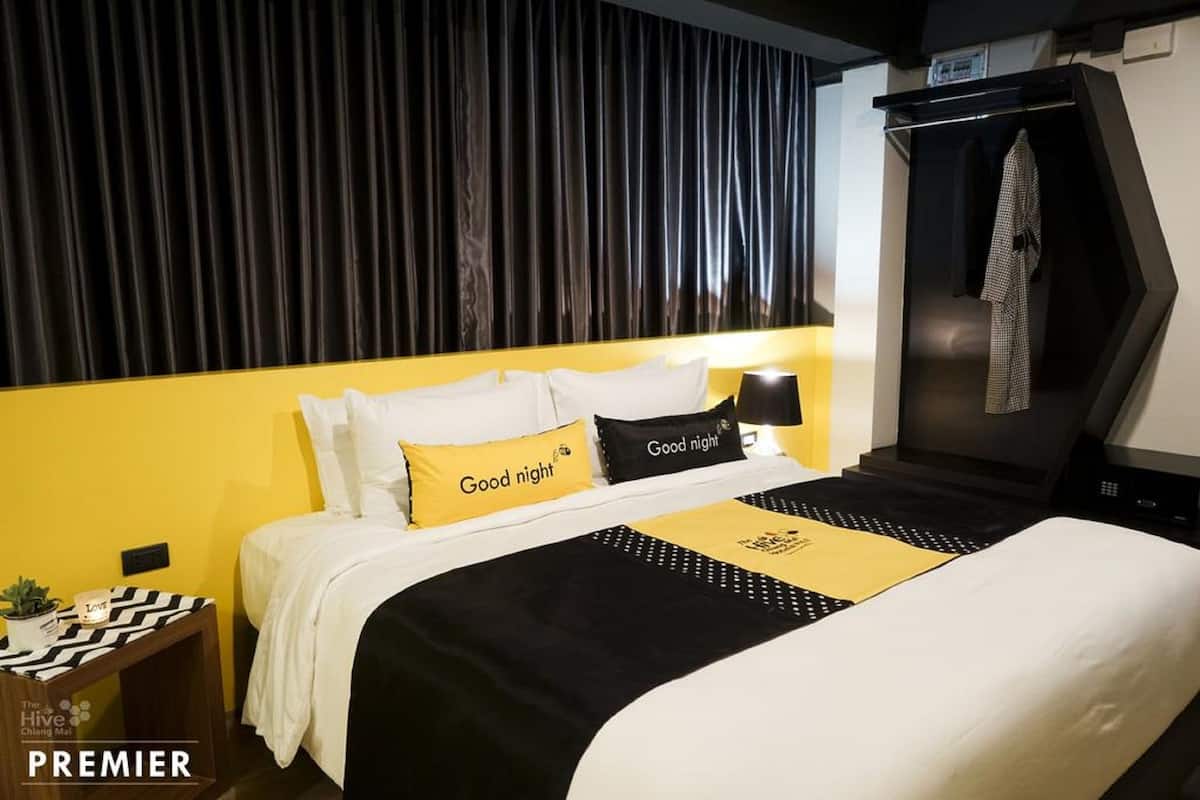 Una habitación de hotel con una cama, una colcha negra y amarilla, un cabecero negro y un armario negro.