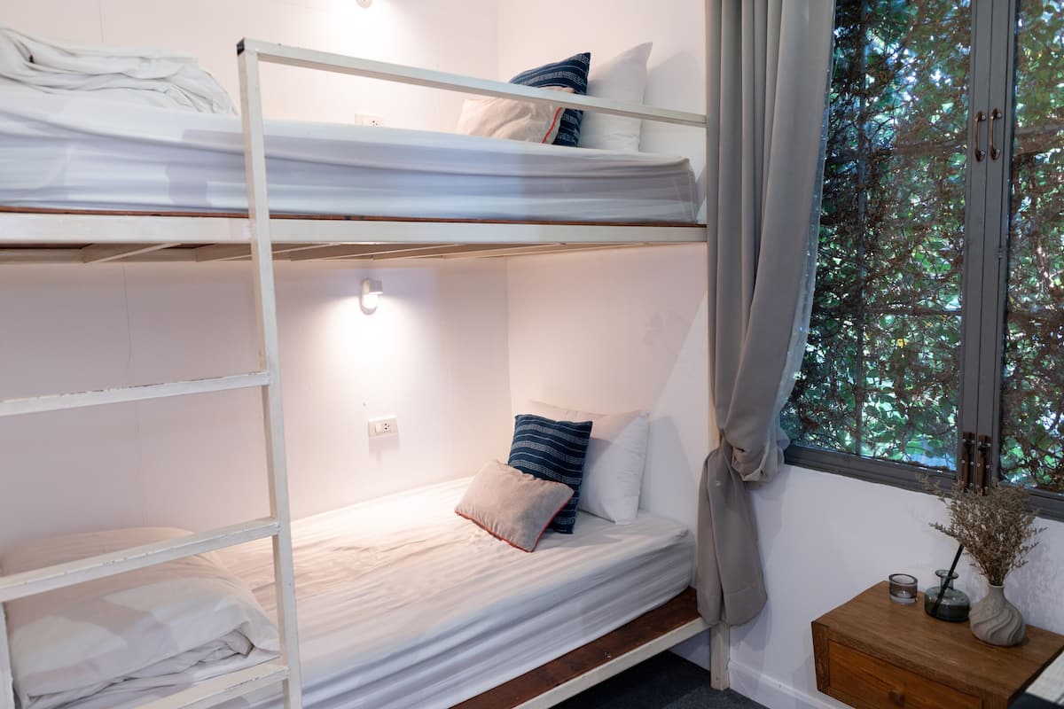 A bunk bed room with a window, a bedside table, and a nightstand.