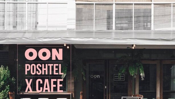 Una cafetería llamada 'OON POSHTEL X CAFE' con terraza y un cartel que indica que está abierta.