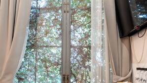 Una habitación con un ventanal grande, una mesita de madera con un florero y velas, y un televisor instalado en la pared.