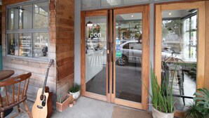 Un escaparate con fachada de madera, una guitarra apoyada en la pared y plantas en macetas al frente.