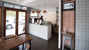 Interior moderno de una cafetería con mostrador, zona de estar y vista a la calle.