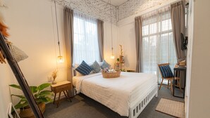Un dormitorio con cama, mesitas de noche, una silla, un escritorio y un ventanal grande.