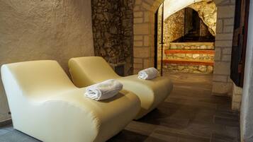 Un área de spa con dos sillones de masaje color beige, una pared de piedra y un banco de madera.