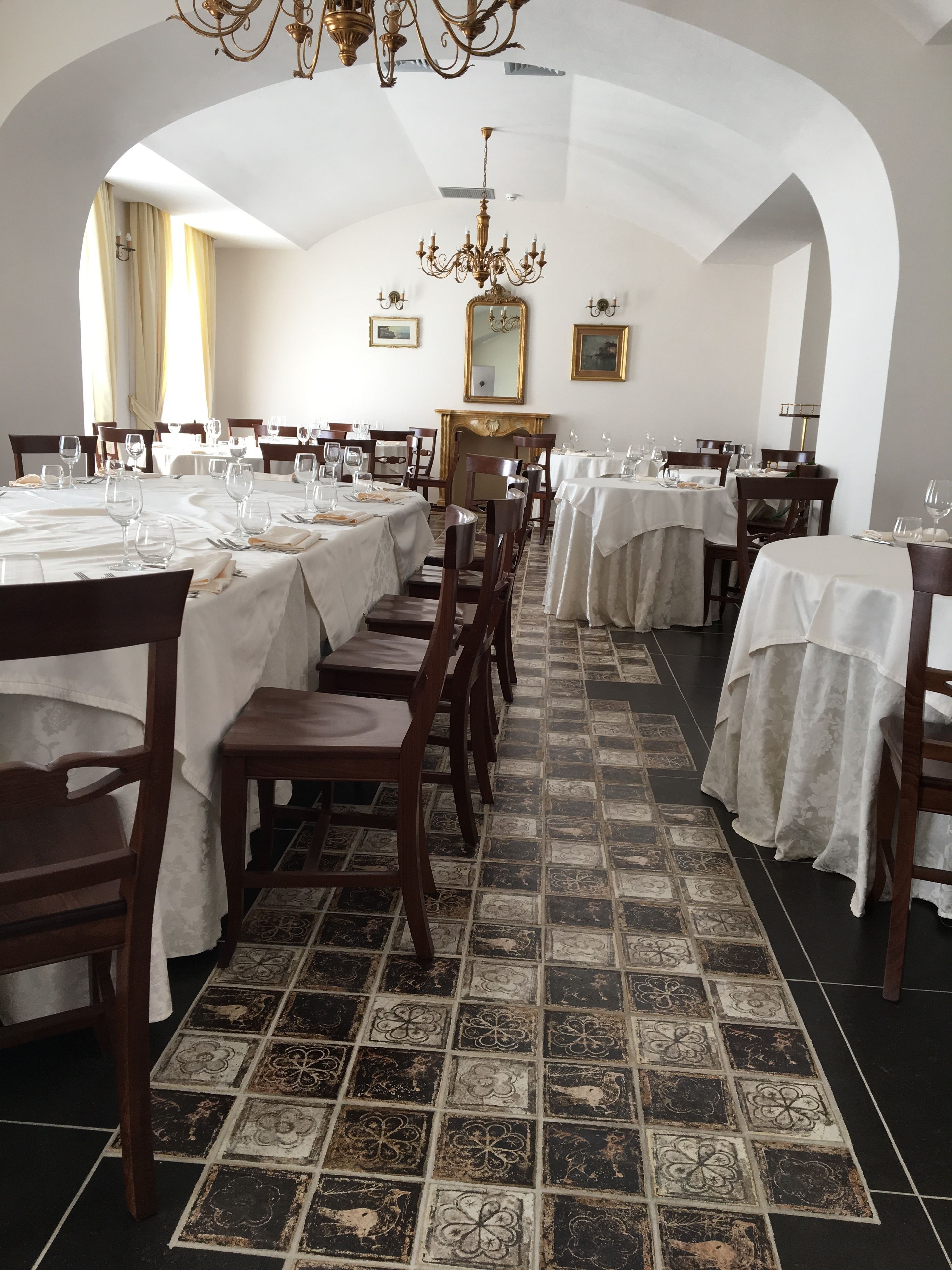 Un restaurant avec de nombreuses tables dressées pour le service, un lustre et un sol carrelé.